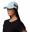 A woman in a light blue Columbia Tech Shade II Cap, featuring mesh side panels for moisture-wicking, and a black t-shirt, faces left against a plain white background.
