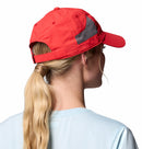 A woman with long blonde hair in a ponytail is shown from behind wearing a red Columbia Tech Shade II Cap and a light blue shirt, set against a white background.