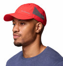 A man in a bright red Columbia Tech Shade II Cap, a lightweight hiking hat with mesh panels, and a blue t-shirt faces slightly left against a white background.