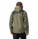 A man is shown from the back wearing a Columbia Mens Whistler Peak Waterproof Shell Jacket in olive green with dark gray accents, standing against a plain white background.