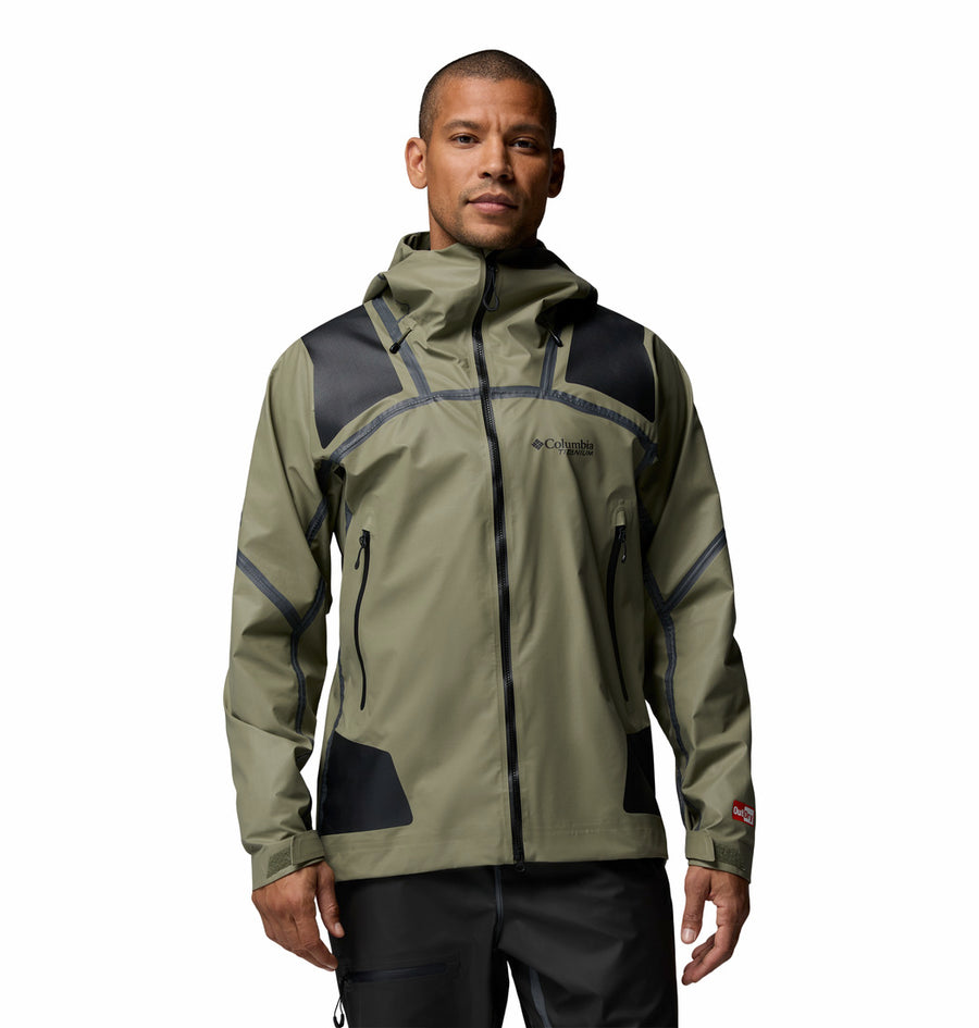 A man wears the Columbia Mens Whistler Peak Waterproof Shell Jacket in light olive green and black, featuring a hood, front zipper, and zippered pockets—ideal for hiking—standing against a plain white background.