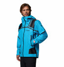 A man wears the Columbia Mens Whistler Peak Waterproof Shell Jacket in bright blue and black, stands angled to the side with his right hand in his pocket, set against a plain white background.