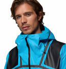A young man with light brown hair and light facial hair wears the Columbia Mens Whistler Peak Waterproof Shell Jacket in bright blue and black, looking confidently at the camera against a plain white background.