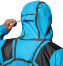 A man wearing the Columbia Mens Whistler Peak Waterproof Shell Jacket in bright blue adjusts the hood using a small blue tab on the back. The jacket features black seams and panels, showcasing its highly weather-resistant design.
