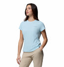 A woman stands against a white background, wearing Columbias Womens Zero Rules Light Technical T-shirt in light blue and beige pants, with one hand in her pocket—ready for hiking with sweat-activated cooling comfort.