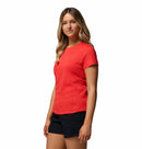 A woman with long, wavy blonde hair stands against a white background wearing the Columbia Womens Zero Rules Light Technical T-shirt in bright red and black shorts. The shirt features sweat-activated cooling, ideal for hiking or active use.