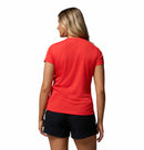 A woman with blonde hair stands with her back to the camera, wearing a Columbia Womens Zero Rules Light Technical T-shirt in red and black shorts, ideal for hiking, against a plain white background.