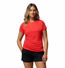 A woman stands against a white background, wearing the Columbia Womens Zero Rules Light Technical T-shirt in bright red and black shorts—ideal for hiking—with one hand in her pocket and a relaxed expression.