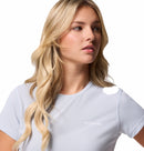 A woman with long, wavy blonde hair wears the Columbia Womens Zero Rules Light Technical T-shirt in light blue, perfect for hiking, and gazes off to the side against a plain white background.