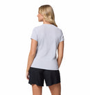 A woman with blonde hair stands facing away against a plain white background, wearing the Columbia Womens Zero Rules Light Technical T-shirt in light gray and black shorts.