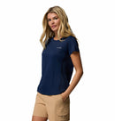 A woman with long blonde hair wears the Columbia Womens Zero Rules Light Technical T-shirt in navy and tan shorts with pockets, posing with one hand in her pocket against a white background—ideal for hiking or sweat-activated cooling.