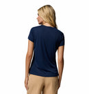 A woman with long blonde hair is seen from behind in a Columbia Womens Zero Rules Light Technical T-shirt (navy blue) and light tan shorts, standing against a plain white background—ideal for hiking or outdoor adventures.