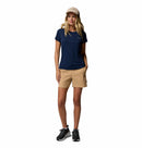 A woman in a beige cap, Columbia Womens Zero Rules Light Technical T-shirt (navy blue), tan shorts, and black sneakers—perfect hiking attire—stands with one hand in her pocket against a white background.