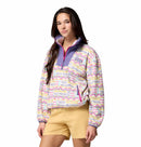A person poses against a white background wearing the Columbia Womens Sequoia Grove™ Printed Half Zip Fleece, featuring a colorful pattern, purple collar, and yellow shorts. Made from recycled polyester.
