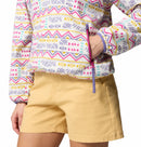A person wears light yellow shorts and a colorful geometric Columbia Womens Sequoia Grove™ Printed Half Zip Fleece, made from recycled polyester, with one hand resting near the pullover’s side zipper pocket.