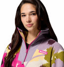 A young woman with long brown hair smiles softly at the camera, wearing Columbias Womens Sequoia Grove™ Printed Half Zip Fleece made from recycled polyester in a colorful floral pattern.