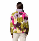 A woman with long brown hair is seen from behind wearing the Columbia Womens Sequoia Grove™ Printed Half Zip Fleece, made from recycled polyester, featuring an abstract floral pattern in purple, green, yellow, and pink.