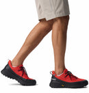 A person in light shorts walks, displaying only their legs and feet in red and black Columbia Mens Tellurix Titanium Outdry Hiking Shoes with Omni‑Max Plus tech, black laces, and a rugged sole for comfort.