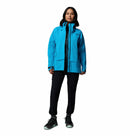 A woman faces forward, wearing the Columbia Womens Saudan Pro™ 3L Shell Jacket in bright blue over a black outfit, paired with black and teal sneakers, set against a plain white background.