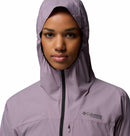 A person faces forward wearing a light purple Columbia Womens Khyex Pro™ Wind Jacket with the hood up and zipped. The ultralight, wind-resistant jacket features the Columbia logo on the left chest.