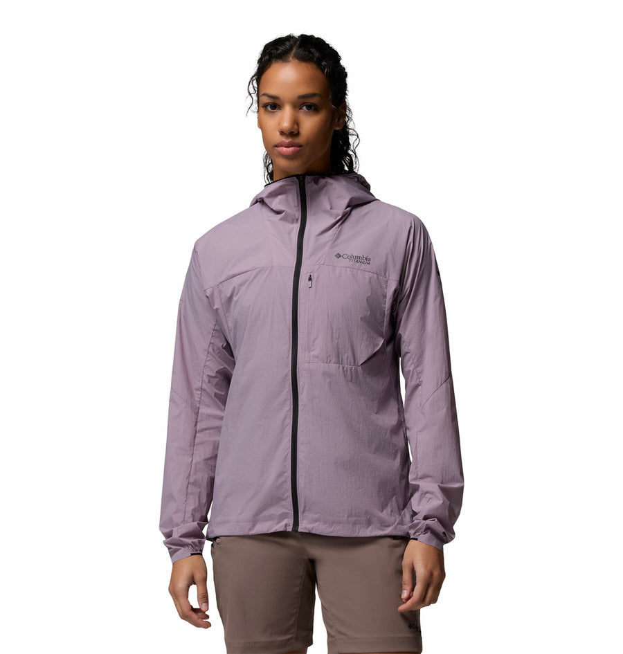 A woman stands facing forward against a white background, wearing the Columbia Womens Khyex Pro™ Wind Jacket in light purple with UPF 50 sun protection and ultralight, wind-resistant design, paired with beige pants.
