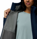 A woman opens her Columbia Womens Trailborne 2.5L Waterproof Shell Jacket, displaying its patterned gray lining and a light blue shirt underneath, with the image highlighting the jackets interior details.