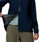 A person wears a blue Columbia Womens Trailborne 2.5L Waterproof Shell Jacket with olive green pants, opening the jacket to show its mesh lining. Only the torso and part of the arms are visible against a white background.