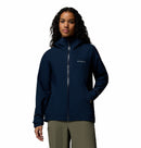 A person with long curly hair models the Columbia Womens Trailborne 2.5L Waterproof Shell Jacket in navy blue, featuring a hood, front zipper, and zippered pockets, standing against a plain white background.