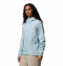 A woman in a light blue Columbia Womens Trailborne 2.5L Waterproof Shell Jacket with a hood and beige pants stands against a white background, looking slightly to the side.