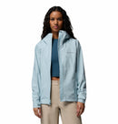 A woman wears a Columbia Womens Trailborne 2.5L Waterproof Shell Jacket in light blue over a teal crop top and beige pants, standing facing forward against a plain white background.