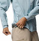 A person wearing Columbia’s Women’s Trailborne 2.5L Waterproof Shell Jacket in light blue and beige pants adjusts the waist drawstring, focusing on their hands and the lower part of this packable rain jacket.