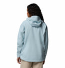 A person with long curly hair is seen from behind wearing the Columbia Womens Trailborne 2.5L Waterproof Shell Jacket in light blue and beige pants, standing against a plain white background.