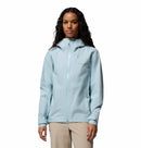 A woman with long curly hair wears the Columbia Womens Trailborne 2.5L Waterproof Shell Jacket in light blue and beige pants, standing facing forward against a plain white background.