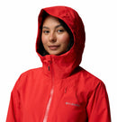 A person wears the Columbia Womens Trailborne 2.5L Waterproof Shell Jacket in bright red, with the hood up and front zipper visible, showcasing the Columbia logo on the chest against a white background.