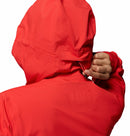 A woman wearing a Columbia Womens Trailborne 2.5L Waterproof Shell Jacket in bright red is shown from behind, adjusting or zipping the hood with her right hand against a white background.