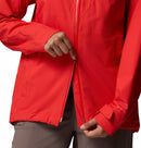 A person, wearing light brown pants, zips up a Columbia Womens Trailborne 2.5L Waterproof Shell Jacket in bright red. Only their torso and hands are visible; the jacket features adjustable cuffs and a visible sleeve seam.