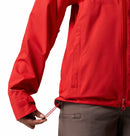 A woman wearing the Columbia Womens Trailborne 2.5L Waterproof Shell Jacket in bright red and brown pants adjusts the hem drawstring with one hand. Only her lower torso and arm are visible.
