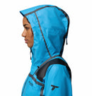 A person in profile wears the Columbia Womens Whistler Peak Waterproof Shell Jacket in bright blue with black accents and a sleeve logo, set against a white background.