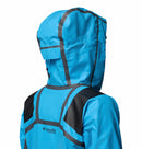 A woman is shown from the back wearing a bright blue Columbia Womens Whistler Peak Waterproof Shell Jacket with a hood up, black taped seams, and black shoulder patches.