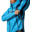 A woman wearing the Columbia Womens Whistler Peak Waterproof Shell Jacket in bright blue unzips a black underarm ventilation zipper, revealing waterproof fabric and seam details. Her face is partly visible against a plain white background.