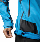 A woman tightens the drawstring at the hem of a bright blue Columbia Womens Whistler Peak Waterproof Shell Jacket, adjusting it around her waist.