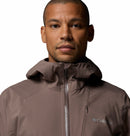 A man in a brown Columbia Mens Trailborne 2.5L Waterproof Shell Jacket with a hood, fully zipped, faces the camera against a plain white background.