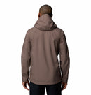 A person facing away from the camera wears a taupe Columbia Mens Trailborne 2.5L Waterproof Shell Jacket and dark pants against a plain white background.