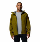 A man with short hair and a neutral expression stands facing forward against a white background, wearing a light gray shirt and the Columbia Mens Trailborne 2.5L Waterproof Shell Jacket in olive green.