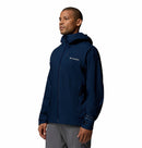 A man wearing a Columbia Mens Trailborne 2.5L Waterproof Shell Jacket in navy blue and gray pants stands against a plain white background, facing slightly to the left.