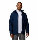 A man faces forward, wearing the Columbia Mens Trailborne 2.5L Waterproof Shell Jacket in navy over a white zip-up shirt and gray pants, set against a plain white background.