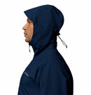 A person in profile wears the Columbia Mens Trailborne 2.5L Waterproof Shell Jacket in navy blue, featuring Omni-Tech fabric, a cinched hood with drawstrings, raised collar, and chest logo. The background is plain white.