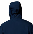 A person is shown from the back wearing a Columbia Mens Trailborne 2.5L Waterproof Shell Jacket in dark blue, with the hood up and a visible drawstring on the hood.