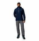 A person wears a light gray cap, Columbia Mens Trailborne 2.5L Waterproof Shell Jacket in navy blue, gray zip-off cargo pants, and blue hiking shoes while standing facing forward against a plain white background.