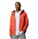A person wearing a bright orange Columbia Mens Trailborne 2.5L Waterproof Shell Jacket over a white button-up shirt and light gray pants stands with one hand in a pocket, posing against a plain white background.